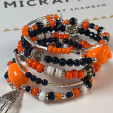 7-layer memory wire bracelet in Halloween theme, featuring orange, black, white, and silver beads with rhinestone spacers and a silver skeleton hand charm. Adjustable and handmade.